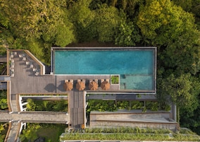 Vista aérea de un complejo turístico con una piscina rectangular grande, una terraza de madera con asientos y una escalera que lleva a una zona en la azotea.