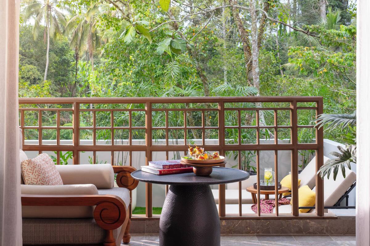 A balcony with a wooden railing, a round table with a bowl and books, and a sofa with cushions.