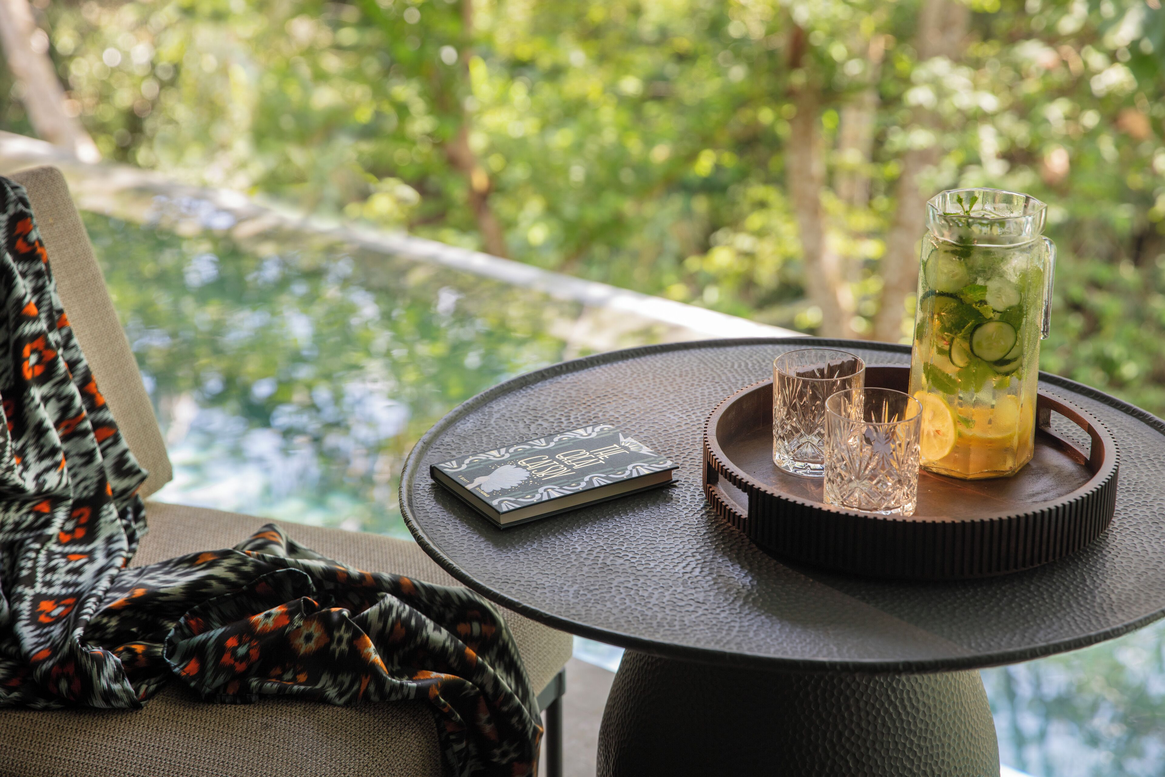 A table with a book, a glass pitcher with a drink, and ice cubes.