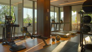 A gym with exercise equipment, large windows, and a view of greenery outside. - Anantara Ubud Bali Resort (Payangan)