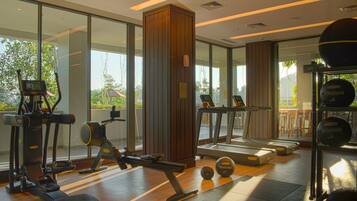 Un gimnasio con equipo de ejercicio, ventanas amplias y vistas a zonas verdes.