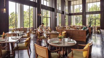 Un restaurante amplio con techos altos y grandes ventanales, que ofrece vistas al exterior. Las mesas están dispuestas con sillas, y se ve a una persona en el fondo.