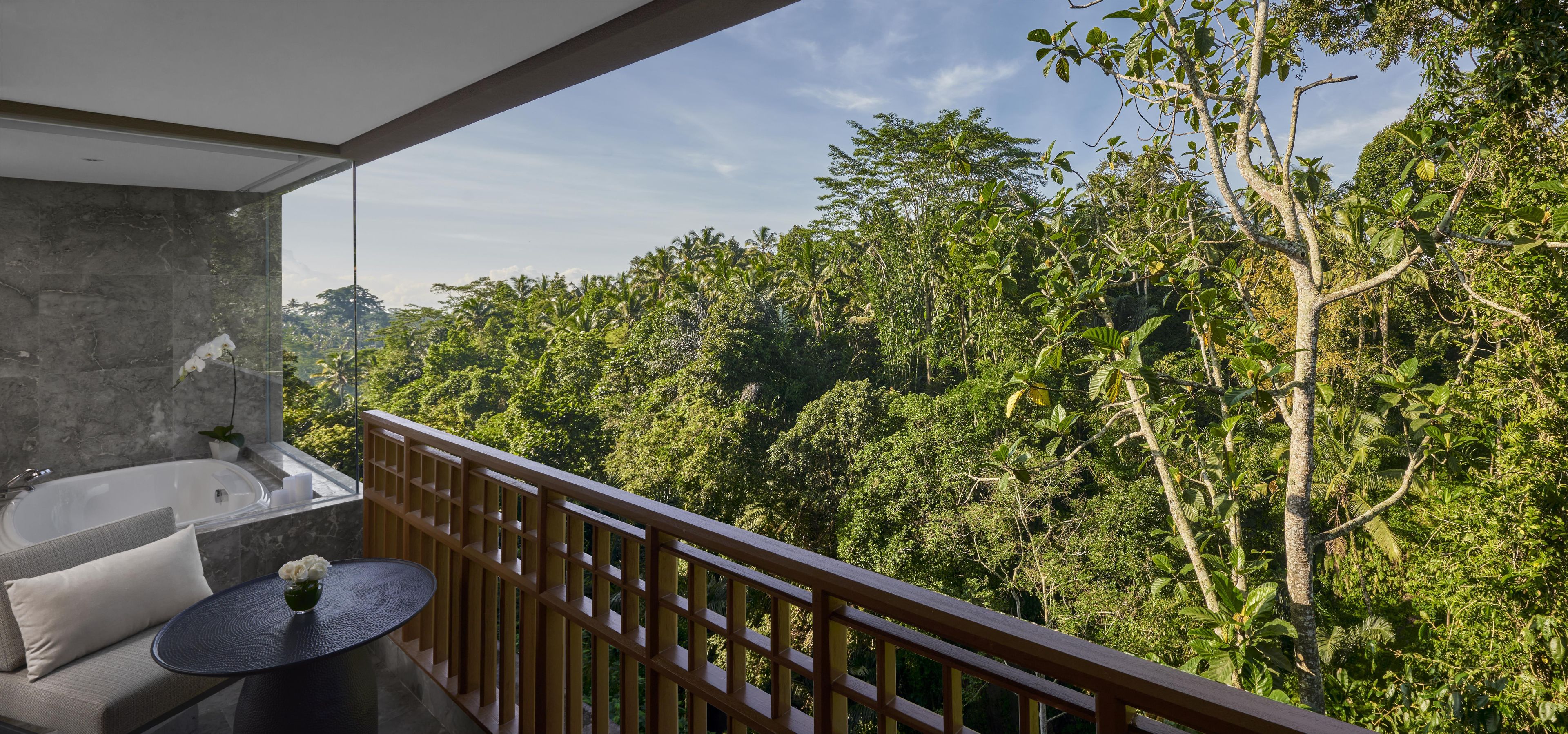 Ein Balkon mit Blick auf einen dichten Wald, einer Marmorwand und einem runden Tisch mit Blumenvase.