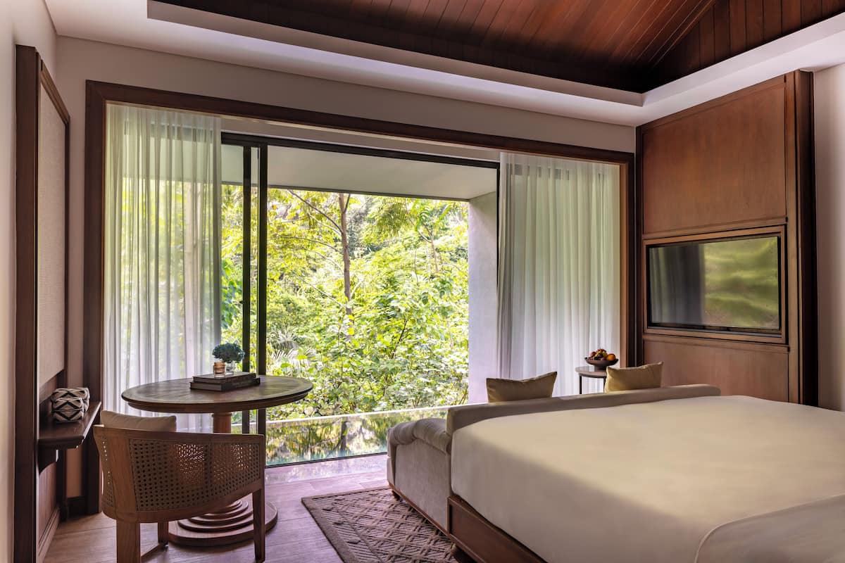 A bedroom with a large bed, a round table with chairs, a small sofa, and a TV mounted on the wall.