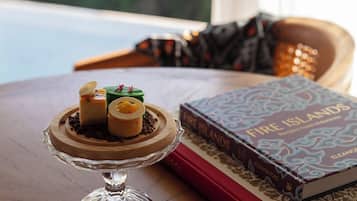 A dessert on a glass stand, a book titled "Fire Islands," and a view of greenery through a window.