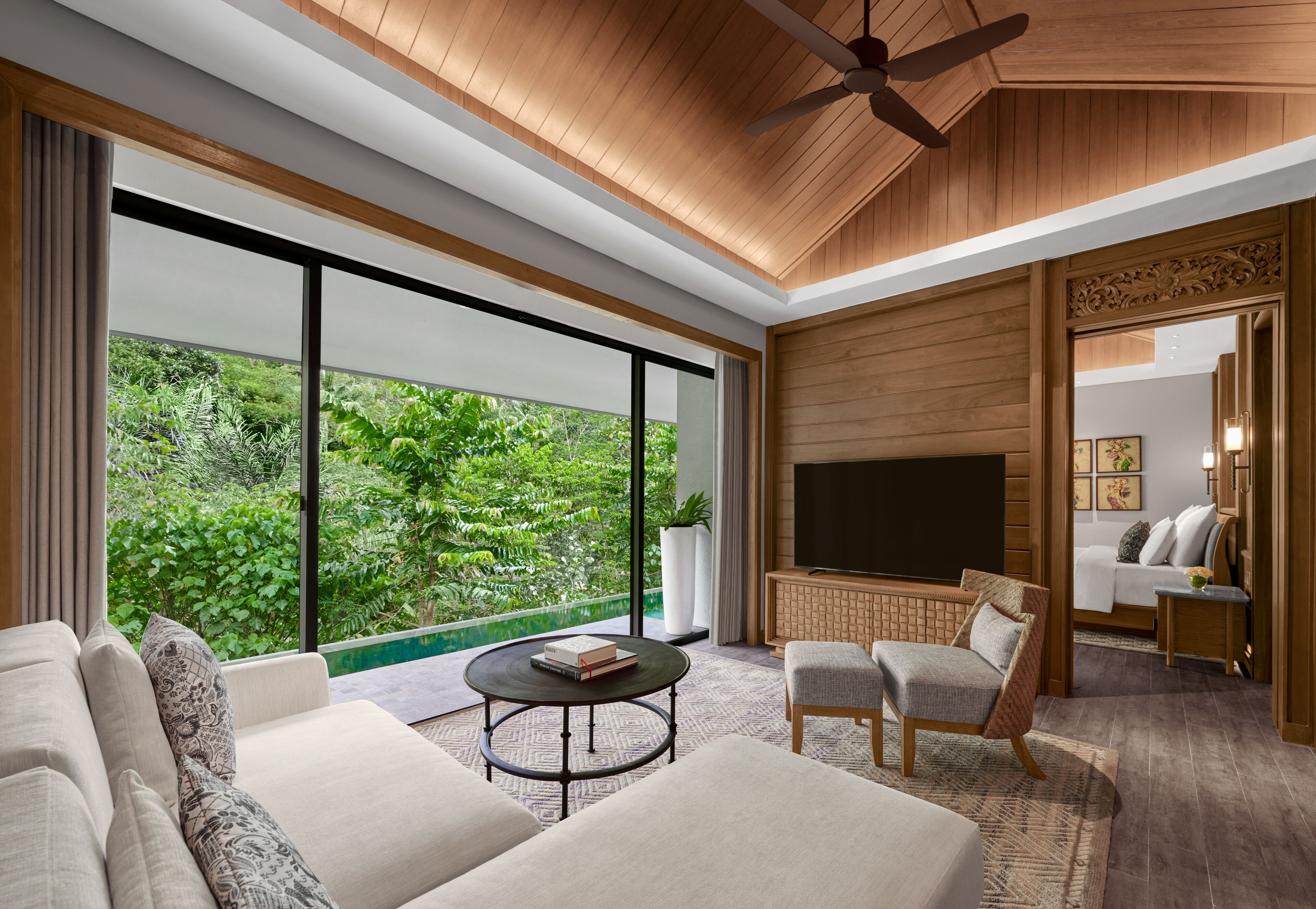 A modern living room with a large TV, comfortable seating, and a view of lush greenery.
