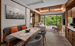 A modern living room with a dining area, a large window with a view of greenery, and a ceiling fan. - Anantara Ubud Bali Resort (Payangan)