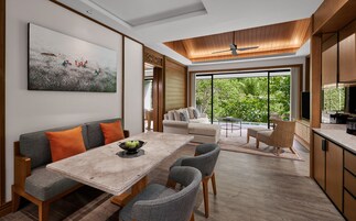 A modern living room with a dining area, a large window with a view of greenery, and a ceiling fan.