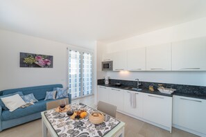 A modern kitchen with white cabinets, a black countertop, and a dining area with a table set for two. - Stylish Residenza TorreBianca 2 Bedroom Apartment sleeps 5 (Lignano Sabbiadoro)