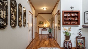 A hallway with wooden flooring, framed artwork on the walls, a small table with a plant, and a shelf with decorative items. - Beautiful house near Columbia Gorge (Gresham)