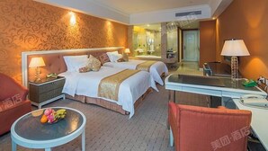 Habitación de hotel con dos camas, un escritorio, una silla, una mesita con fruta y un espejo.