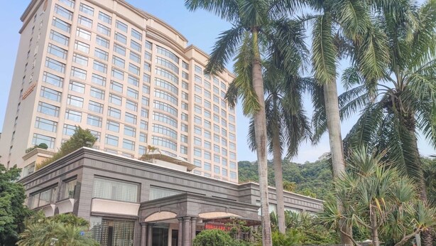 Un hotel con fachada moderna, entrada destacada y jardín ajardinado con palmeras.
