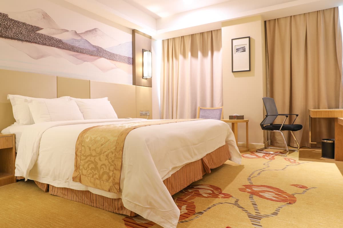 A hotel room with a large bed, a desk, a chair, and a painting on the wall.
