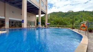 Una piscina con vistas a un edificio y una colina boscosa al fondo.