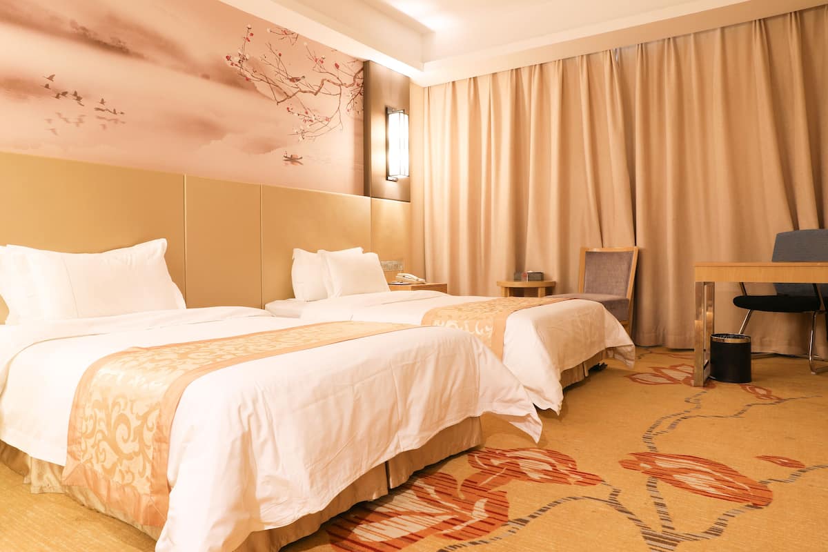 A hotel room with two beds, a desk, a chair, a trash can, and a wall with a nature-themed mural.