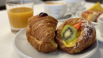 Une table dressée pour le petit-déjeuner, avec des croissants, un verre de jus d’orange et une tasse de café.