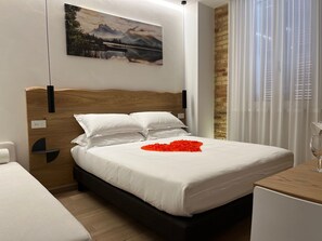 A neatly made bed with white linens and a red heart decoration, a wooden headboard, a painting of a landscape, and a window with curtains. - Civitaloft (Civitanova Marche)
