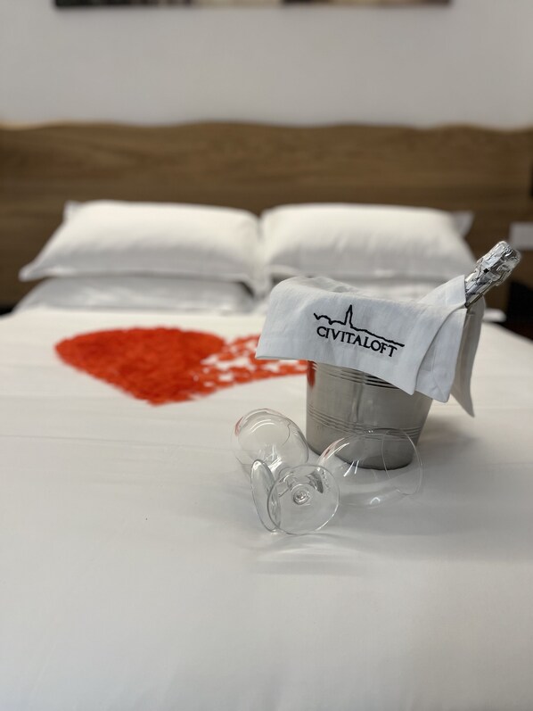 A bed with a white sheet, a bucket with a label, and a heart-shaped stain. - Civitaloft (Civitanova Marche)
