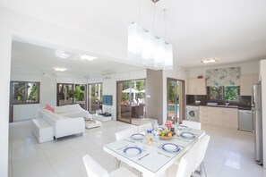 A modern kitchen with white cabinets, a stainless steel refrigerator, and a dining area with a glass table set for four.