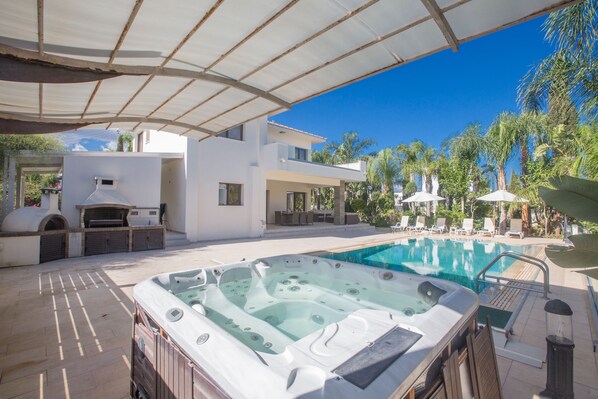 A pool area with a hot tub, outdoor seating, and a covered patio.
