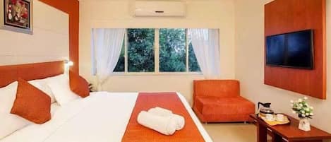 Ein Hotelzimmer mit Bett, Sessel, Fernseher und einem Fenster mit Vorhängen.