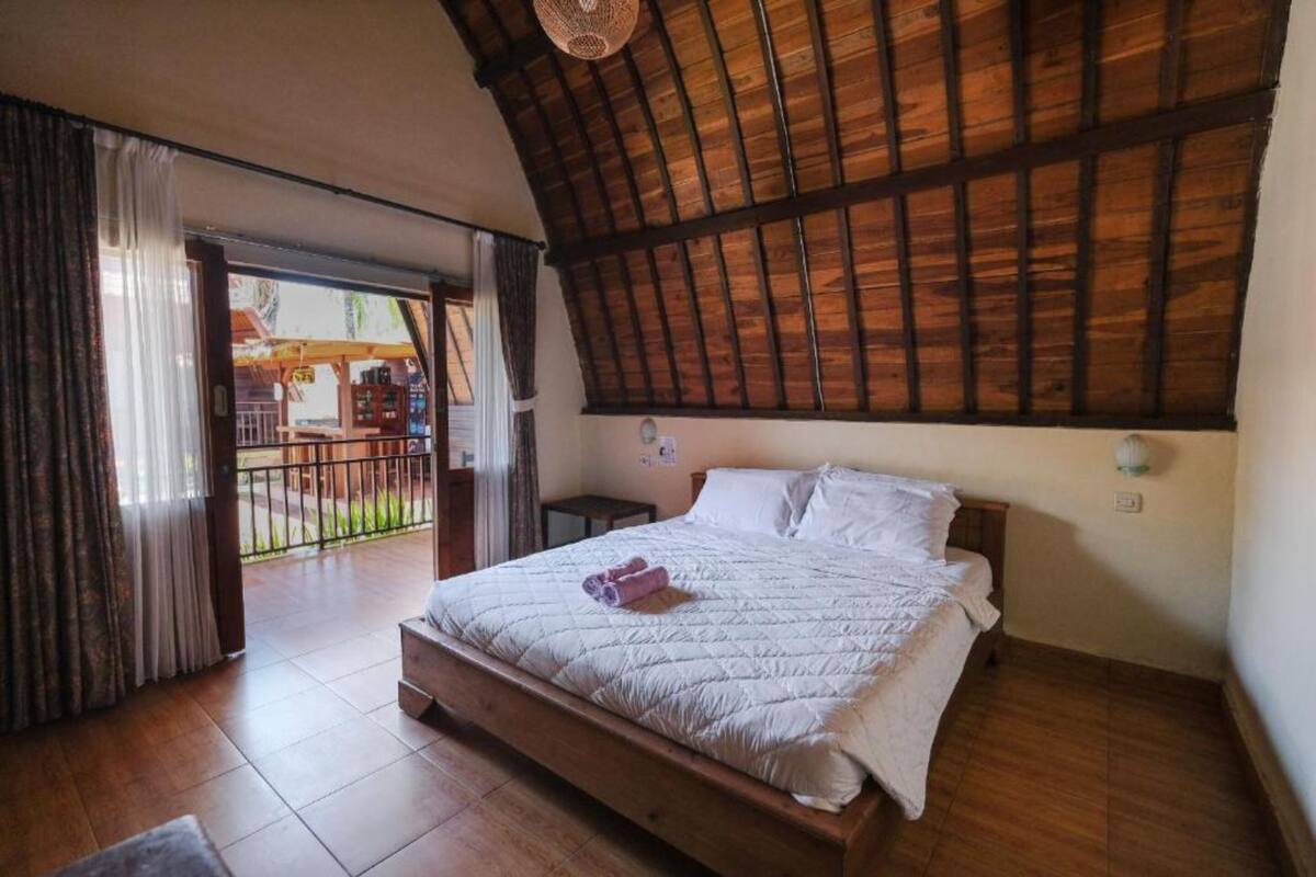A bedroom with a wooden ceiling, a bed with white bedding, and a view of an outdoor area through a glass door.