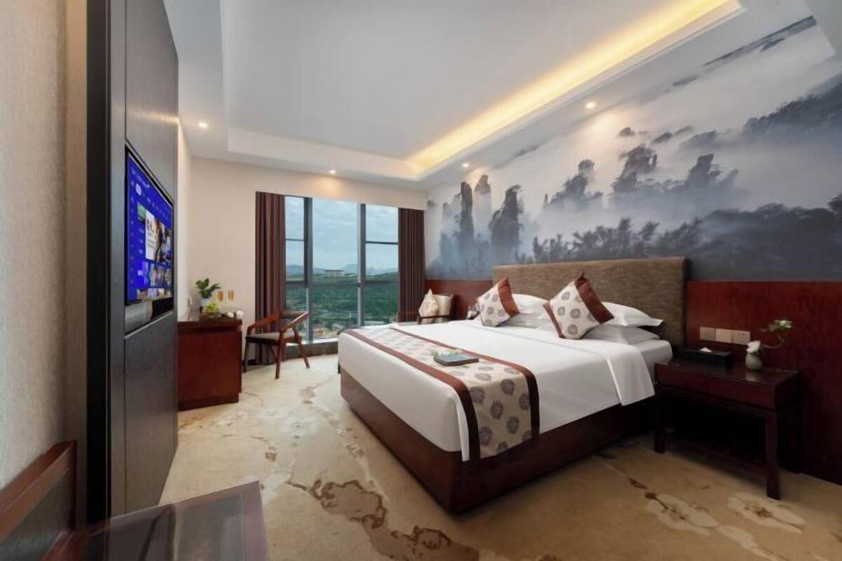 A hotel room with a large bed, a desk, a chair, a TV, and a painting on the wall.