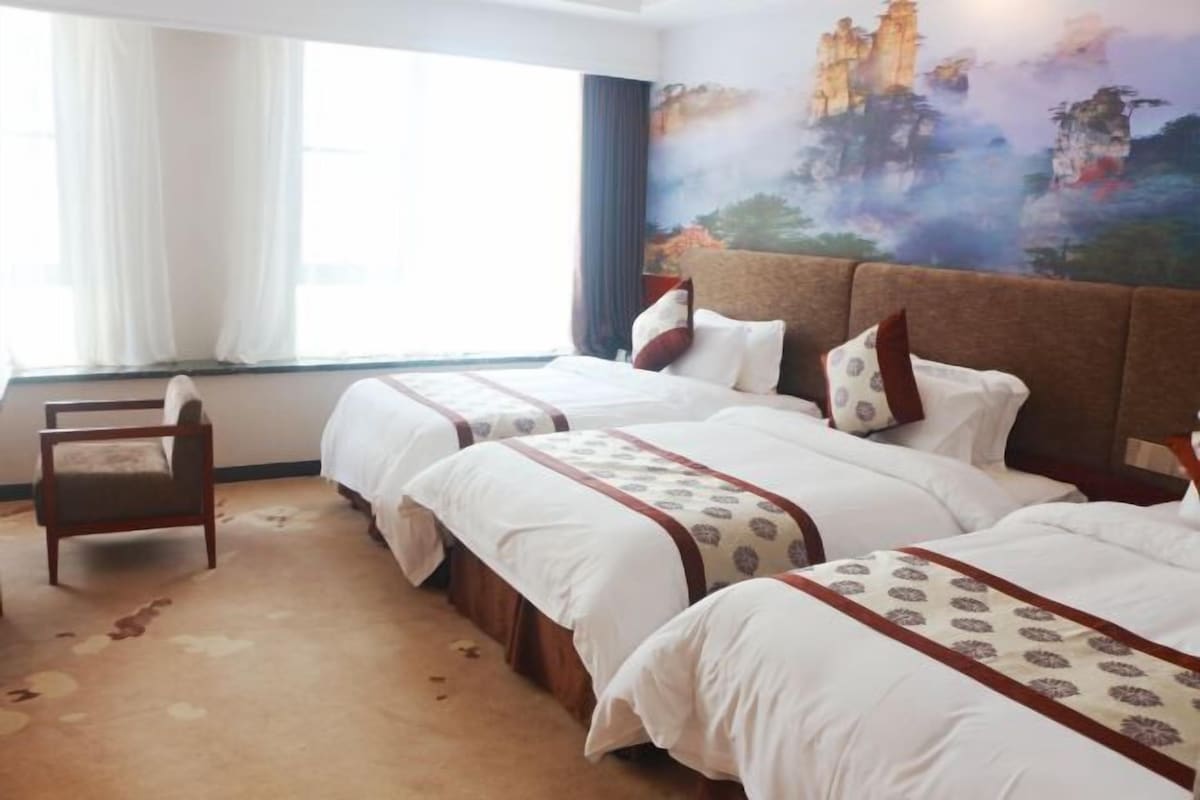 Habitación de hotel con tres camas, un ventanal con cortinas y un mural en la pared.