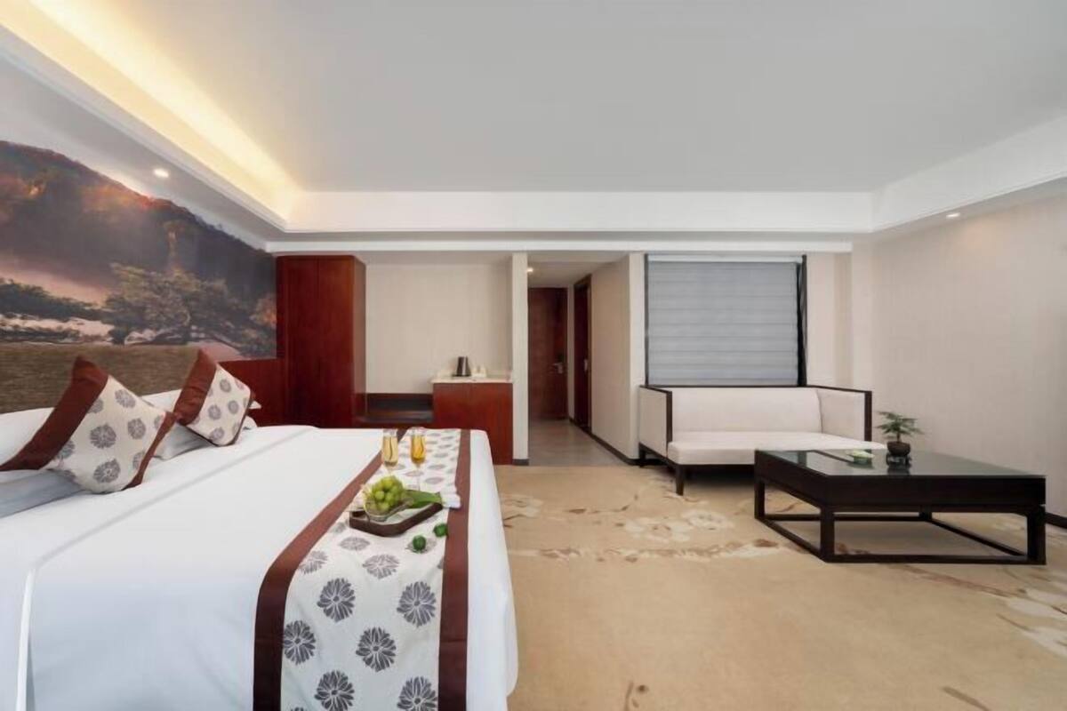 A hotel room with a bed, a sofa, a coffee table, and a view of a mountain landscape.