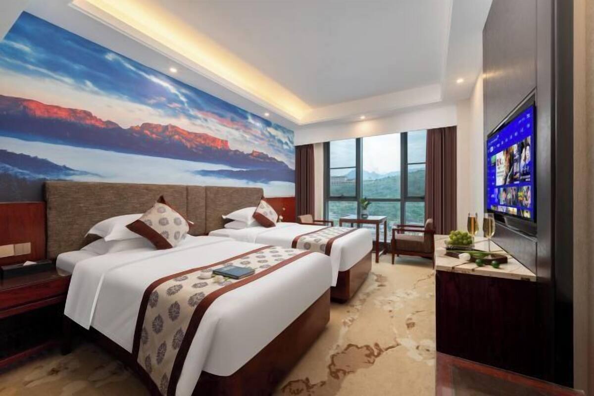 A hotel room with two beds, a large window, a TV, and a desk with a chair.