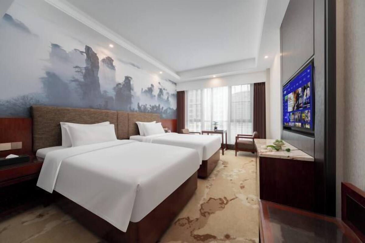A hotel room with two beds, a desk, a TV, and a mural on the wall.