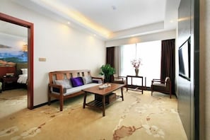 Una habitación de hotel con sofá, mesa de centro, una silla, planta y un ventanal grande.