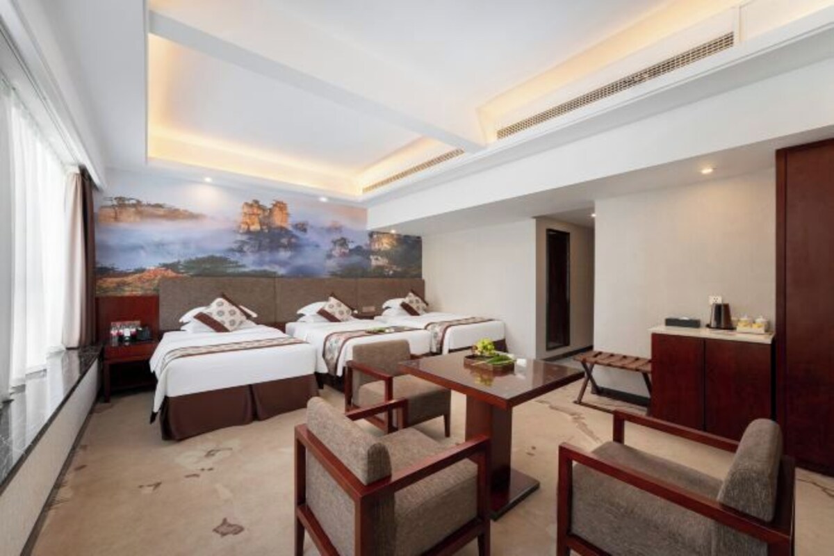 Habitación de hotel con una cama grande, dos camas más pequeñas, una mesa de comedor y un cuadro en la pared.