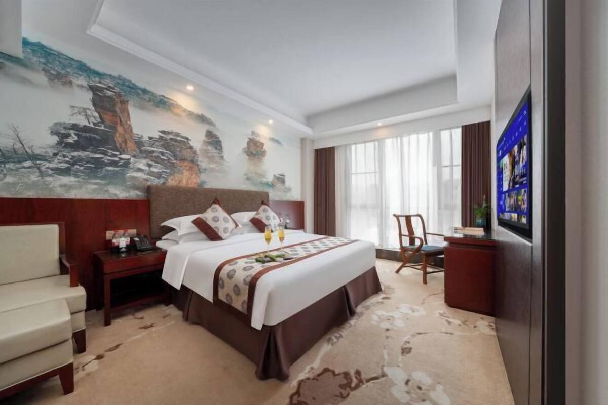 A hotel room with a bed, a desk, a chair, a TV, and a painting on the wall.