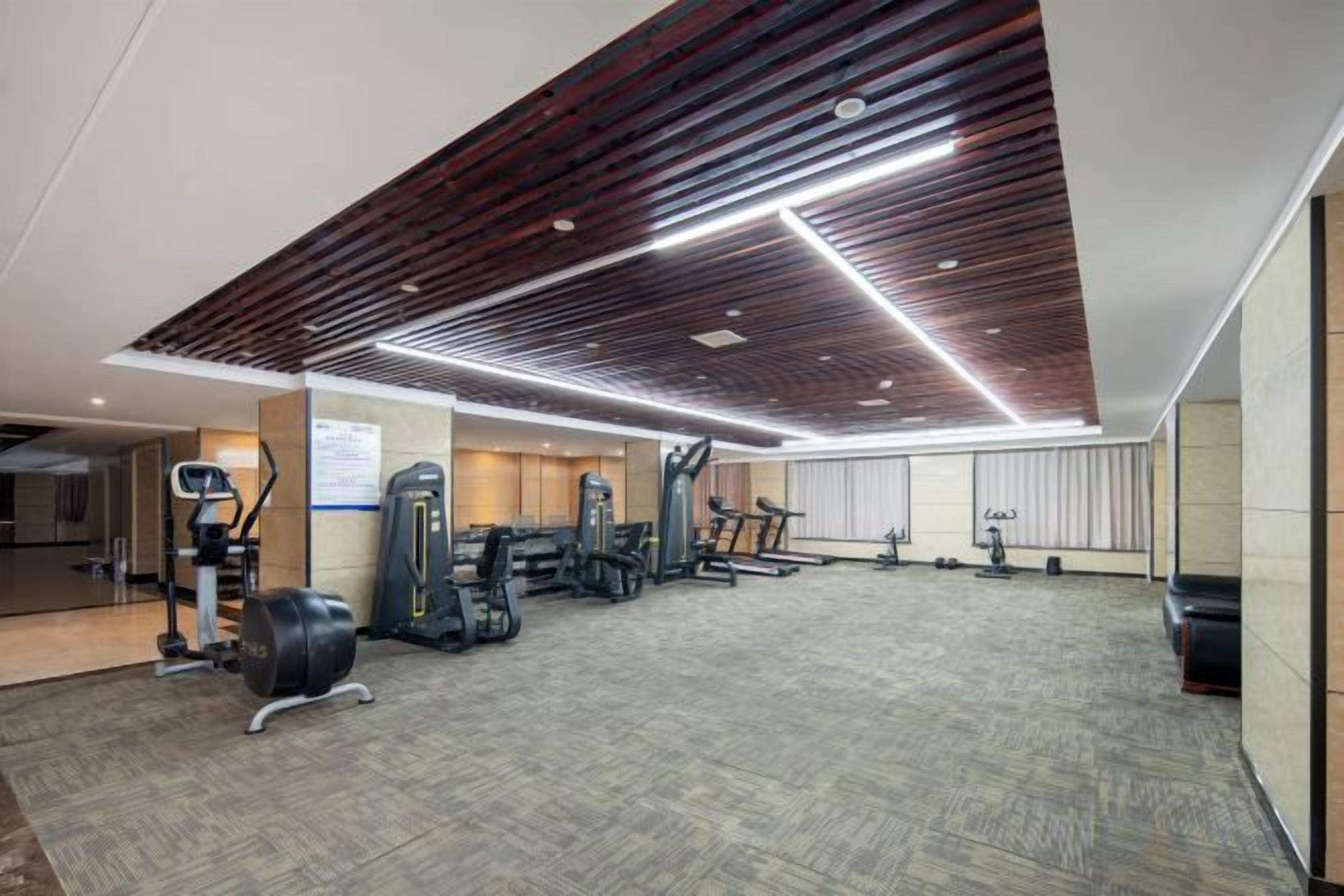 A gym with exercise equipment, a patterned carpet, and a wooden ceiling design.