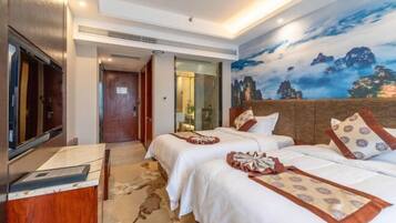 A hotel room with two beds, a flat-screen TV, a wooden desk, and a mural of mountains.