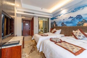 Habitación de hotel con dos camas, un televisor de pantalla plana, un escritorio de madera y un mural de montañas.