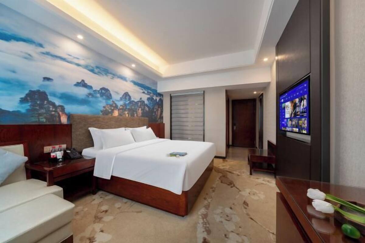 A hotel room with a bed, bedside table, TV, and a painting on the wall.
