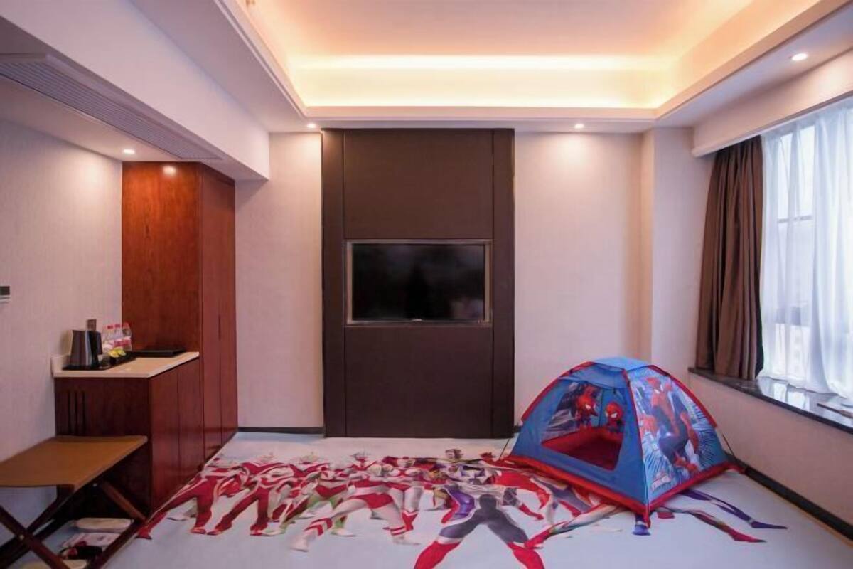 A hotel room with a large bed, a TV, a tent, and a desk with a chair.