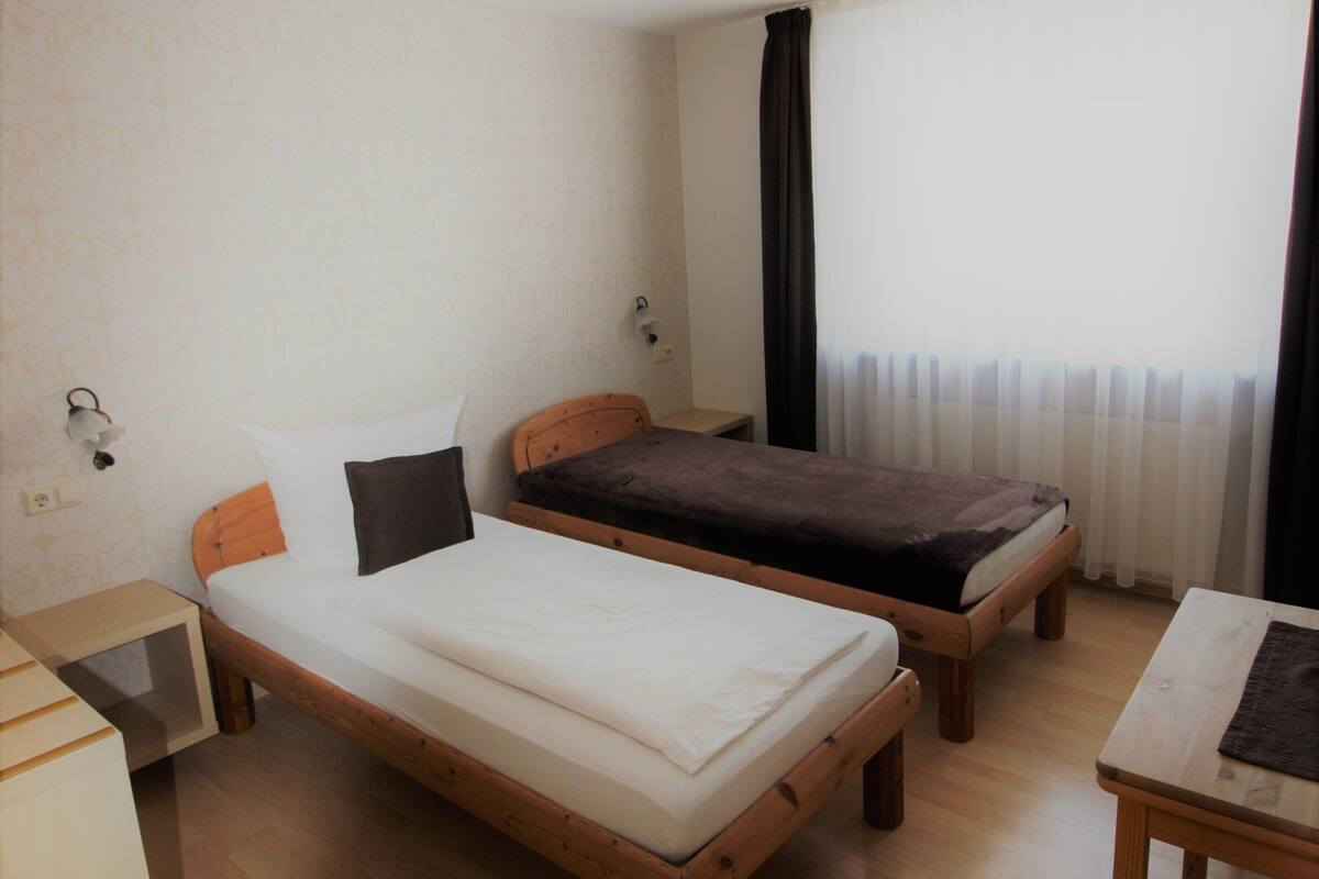 A small, simple room with two single beds, a desk, and a chair.