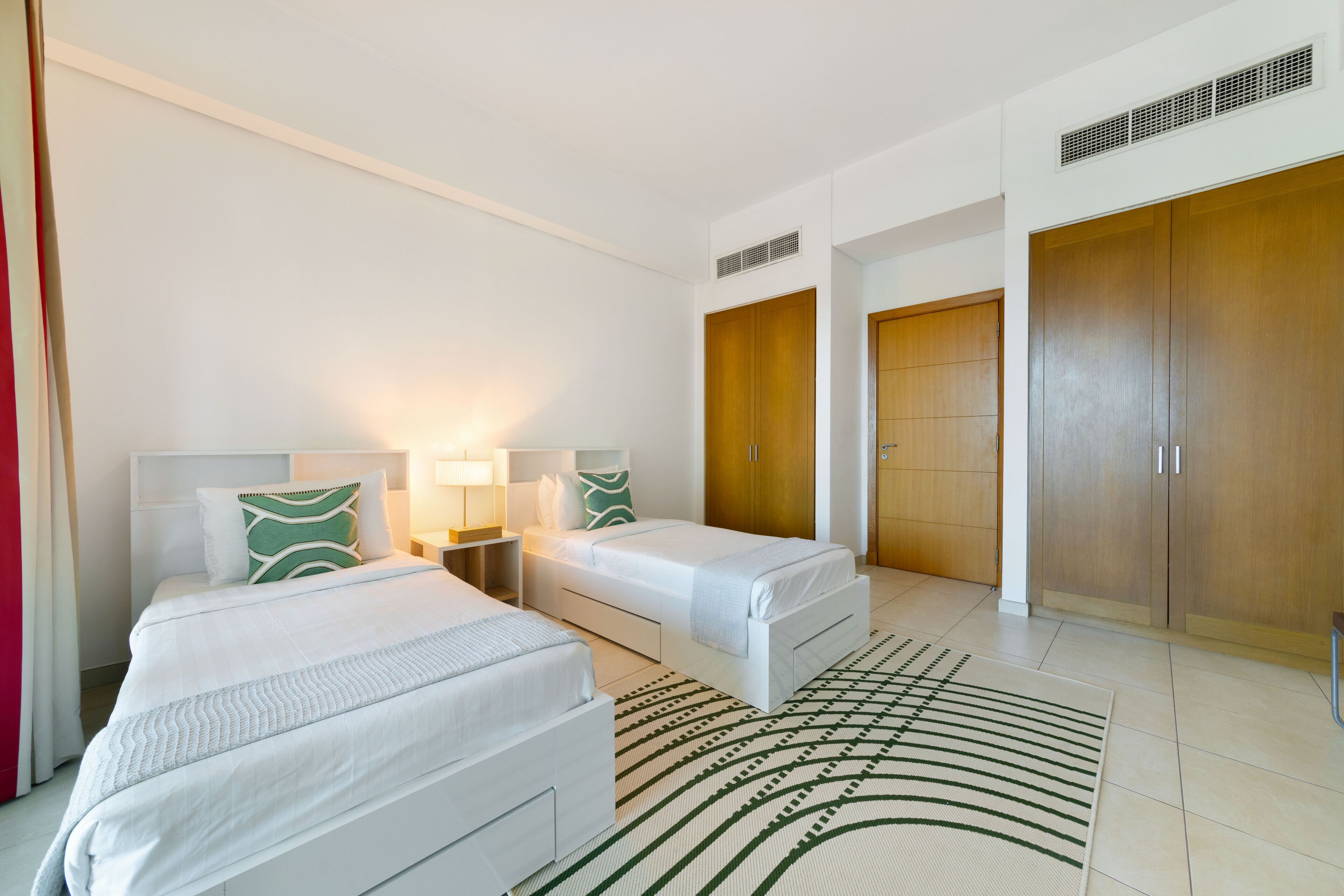 A hotel room with two beds, a large wardrobe, and a patterned rug.