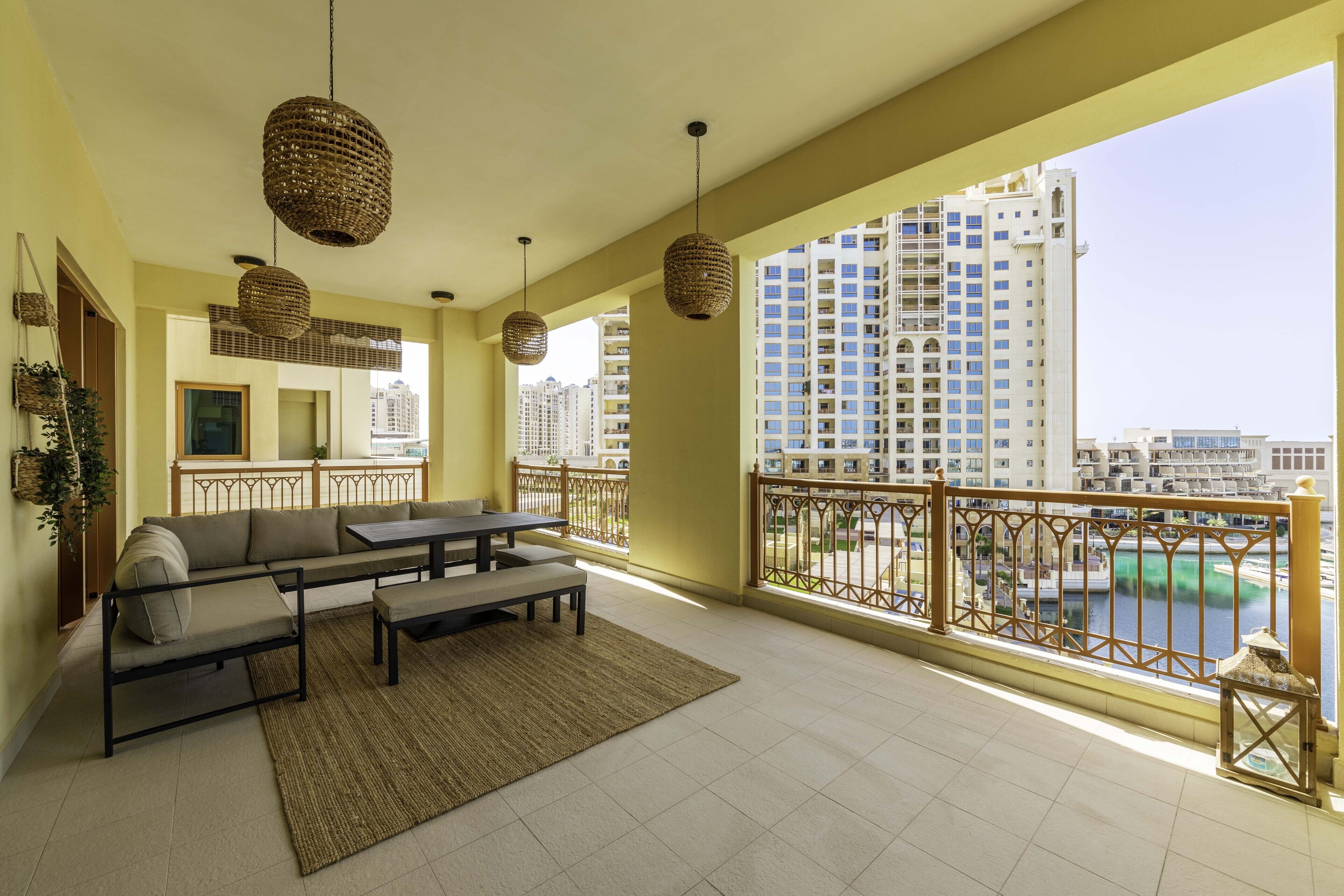 A balcony with a sofa, table, and hanging wicker lamps. It overlooks a cityscape and a body of water.