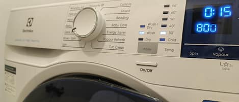 A front view of a front-loading washing machine with a digital display, control panel, and a wool hand wash symbol.
