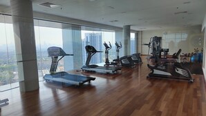 A spacious gym with various exercise equipment, large windows offering a city view, and a high ceiling. - Executive Azure Next to New World Hotel (Petaling Jaya)