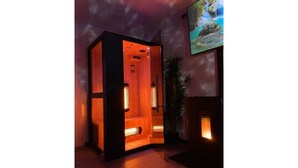 A sauna room with a wooden floor, a glass door, and a wall-mounted TV displaying a waterfall scene.