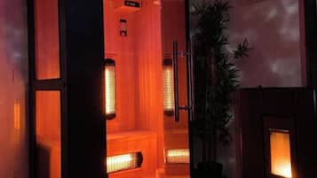 Un sauna con suelo de madera, puerta de vidrio y televisor en la pared mostrando una escena de cascada.