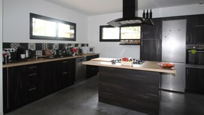 A modern kitchen with dark cabinetry, a central island, and a stainless steel refrigerator. - Pretty wooden house 5 minutes from the ocean (Labenne)