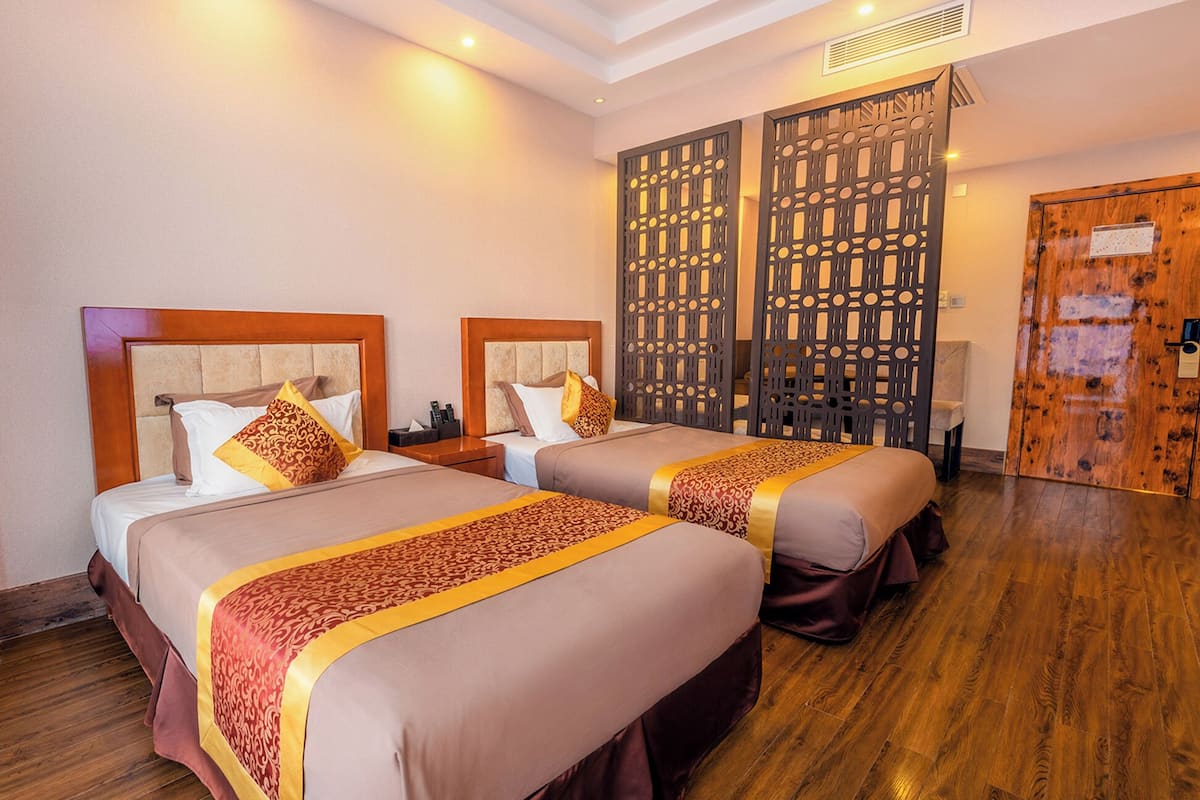 A hotel room with two beds, wooden headboards, and a decorative partition.