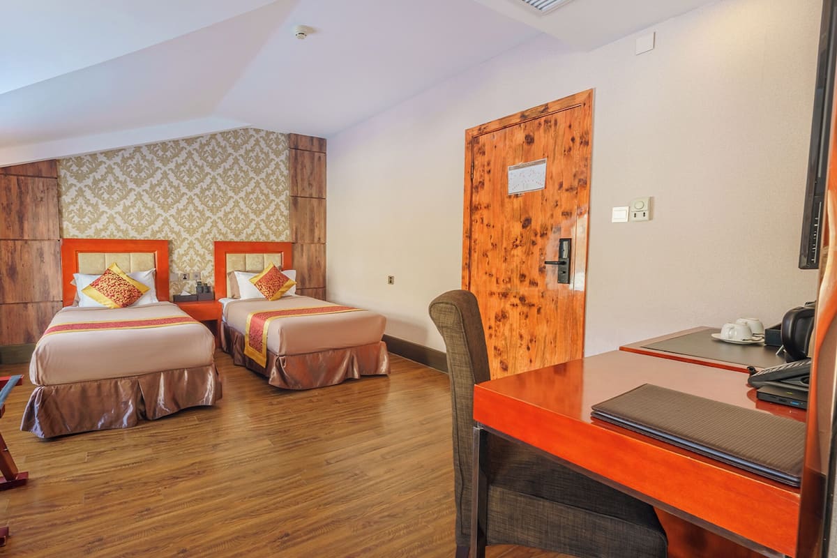 A hotel room with two beds, a wooden desk, and a chair.