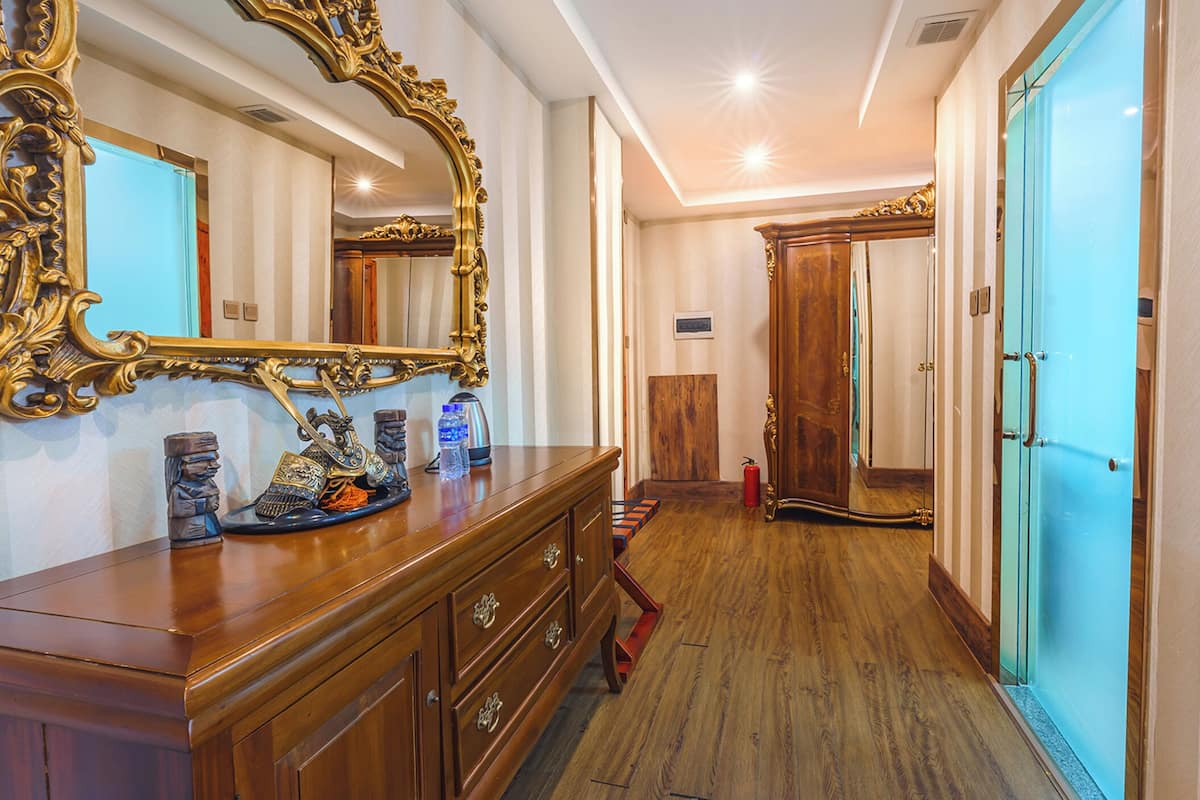 A hallway with a wooden dresser, ornate gold mirrors, and a blue door.